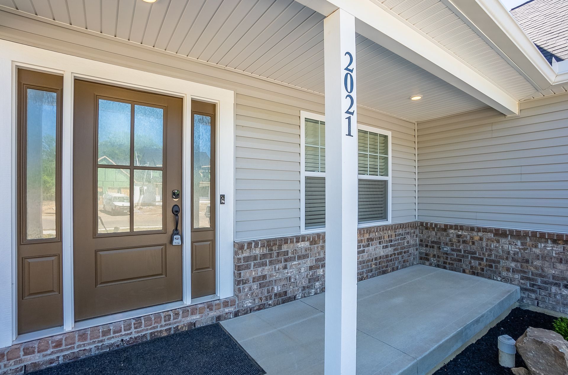 The front door of a house with a porch and a brick wall.