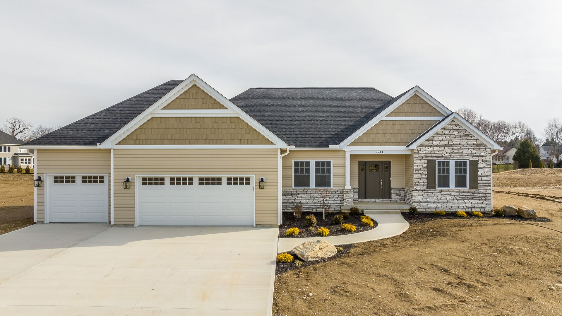 A large house with two garages and a driveway is sitting on top of a dirt field.