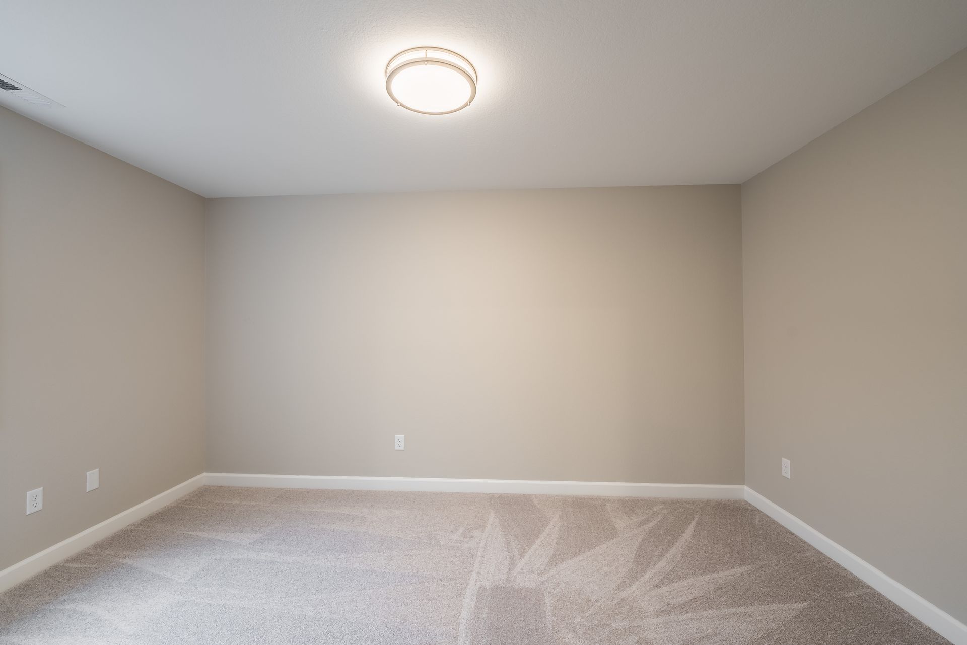 An empty room with a light on the ceiling and a carpeted floor.