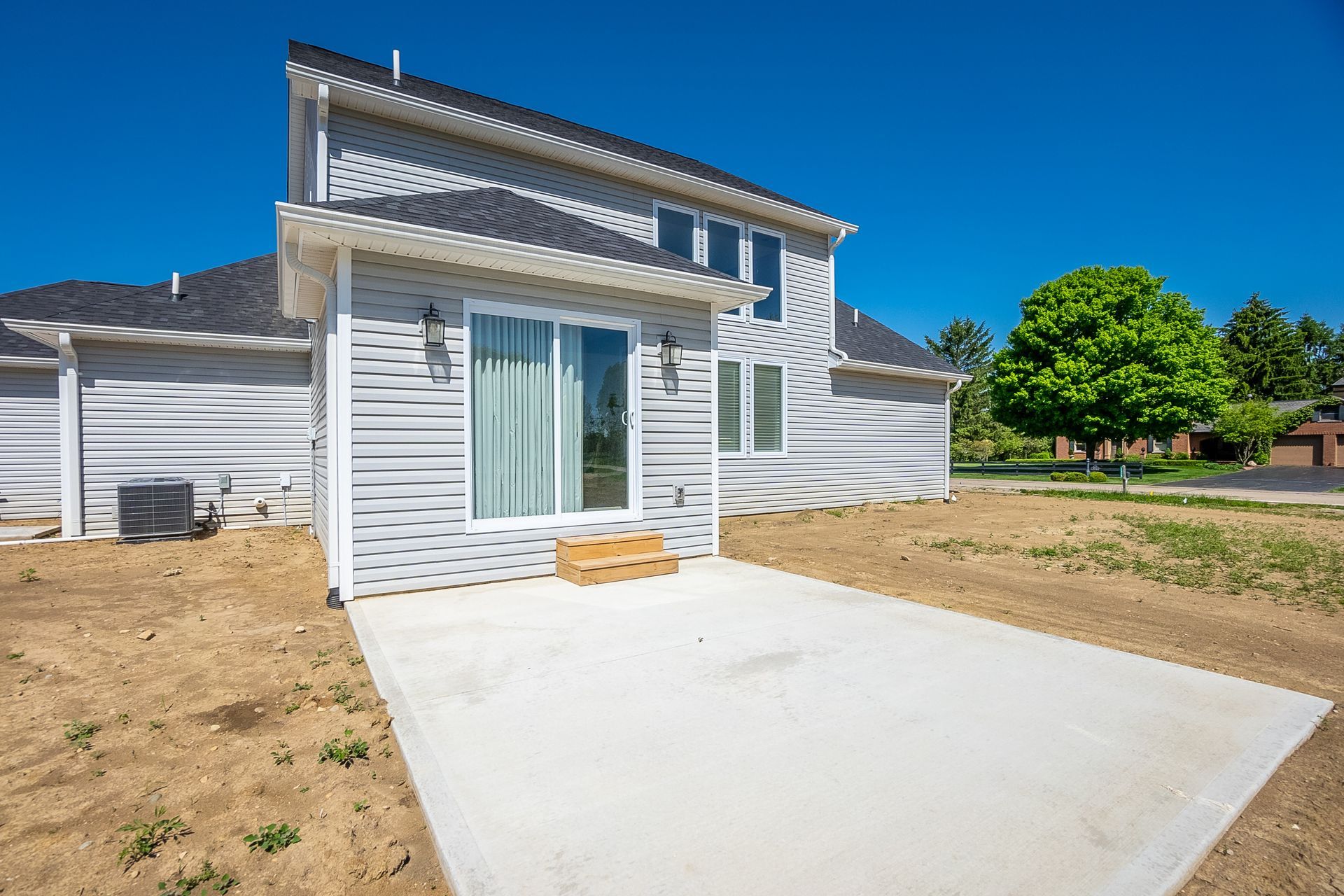 The backyard of a house with a concrete patio and sliding glass doors.