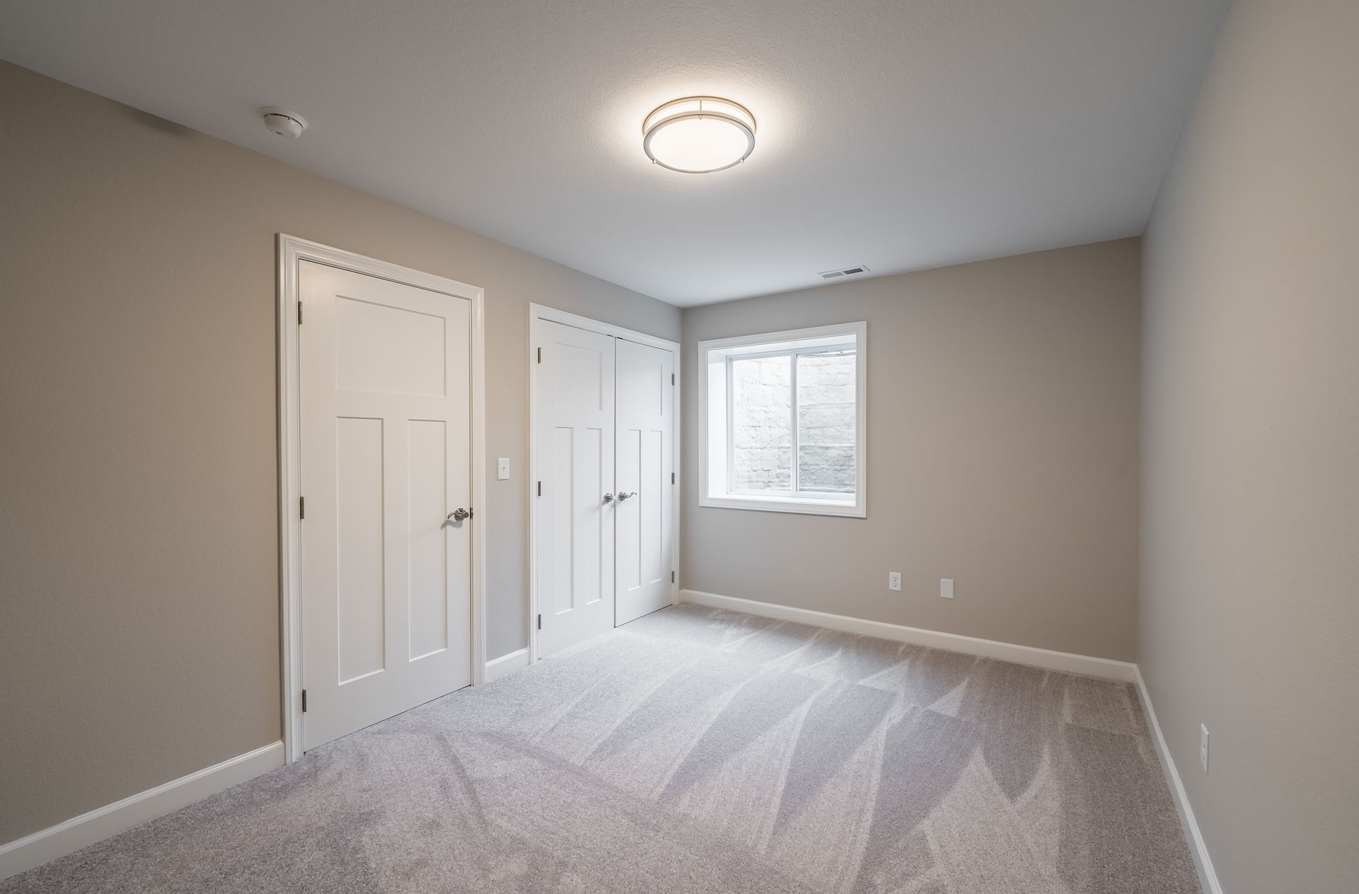 An empty bedroom with a carpeted floor and a window.