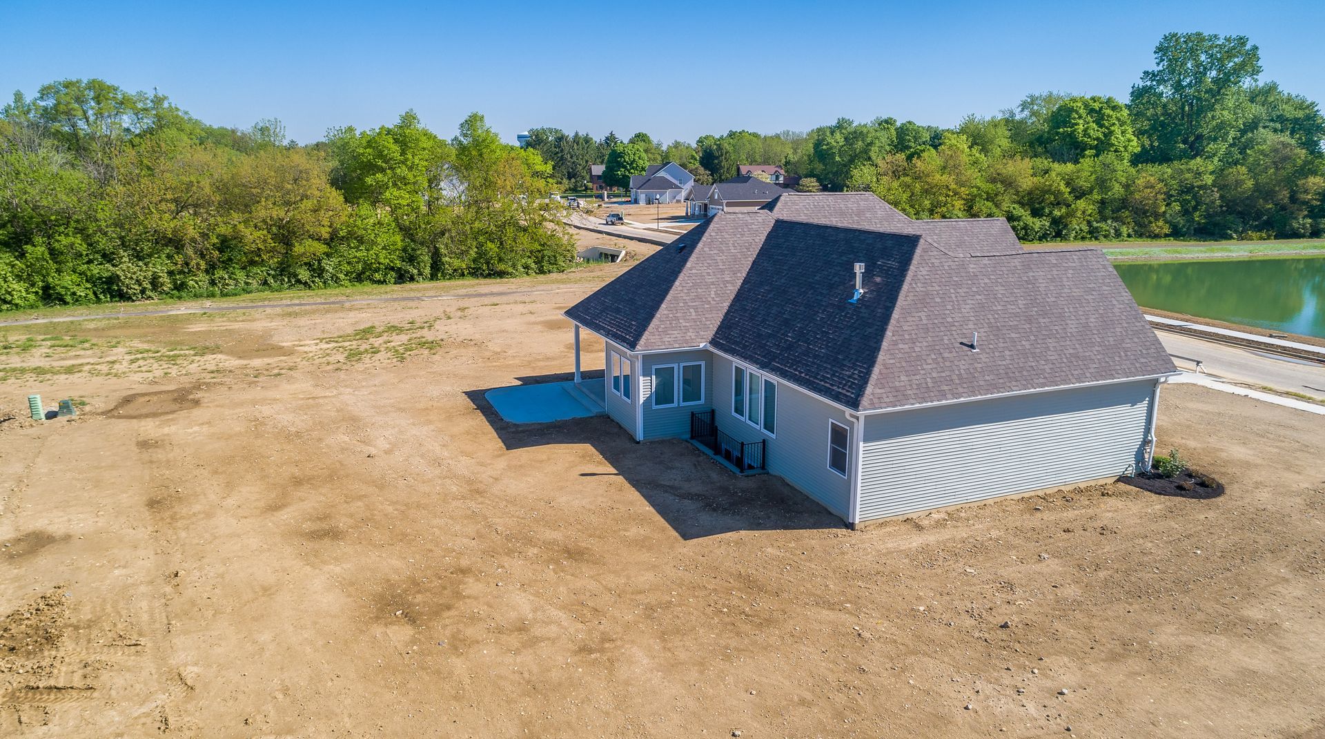 An aerial view of a house sitting on top of a dirt field next to a lake.