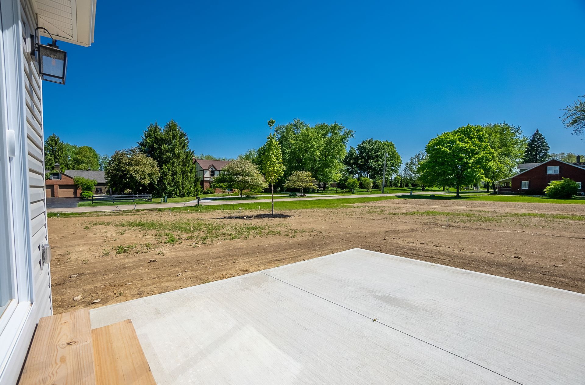 A concrete patio with a view of a dirt field and a house in the background.