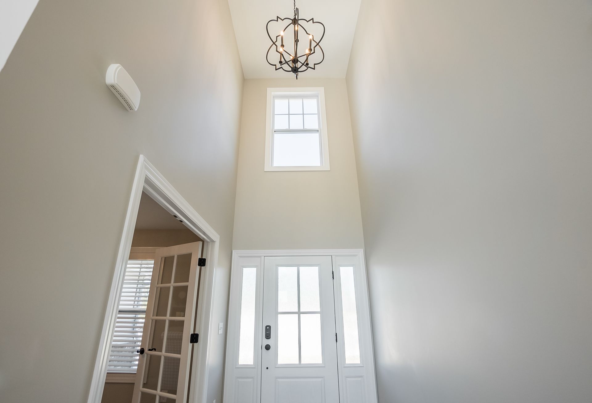 A long hallway with a white door and a chandelier hanging from the ceiling.