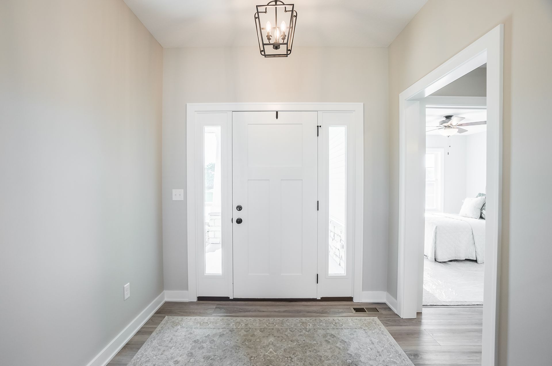 A hallway with a white door and a chandelier hanging from the ceiling.