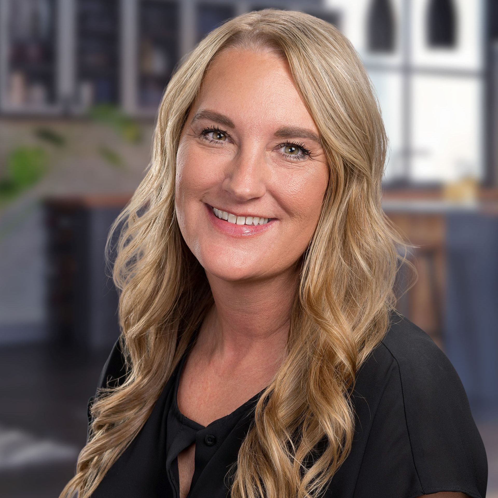 A woman with long blonde hair is smiling for the camera while wearing a black shirt.