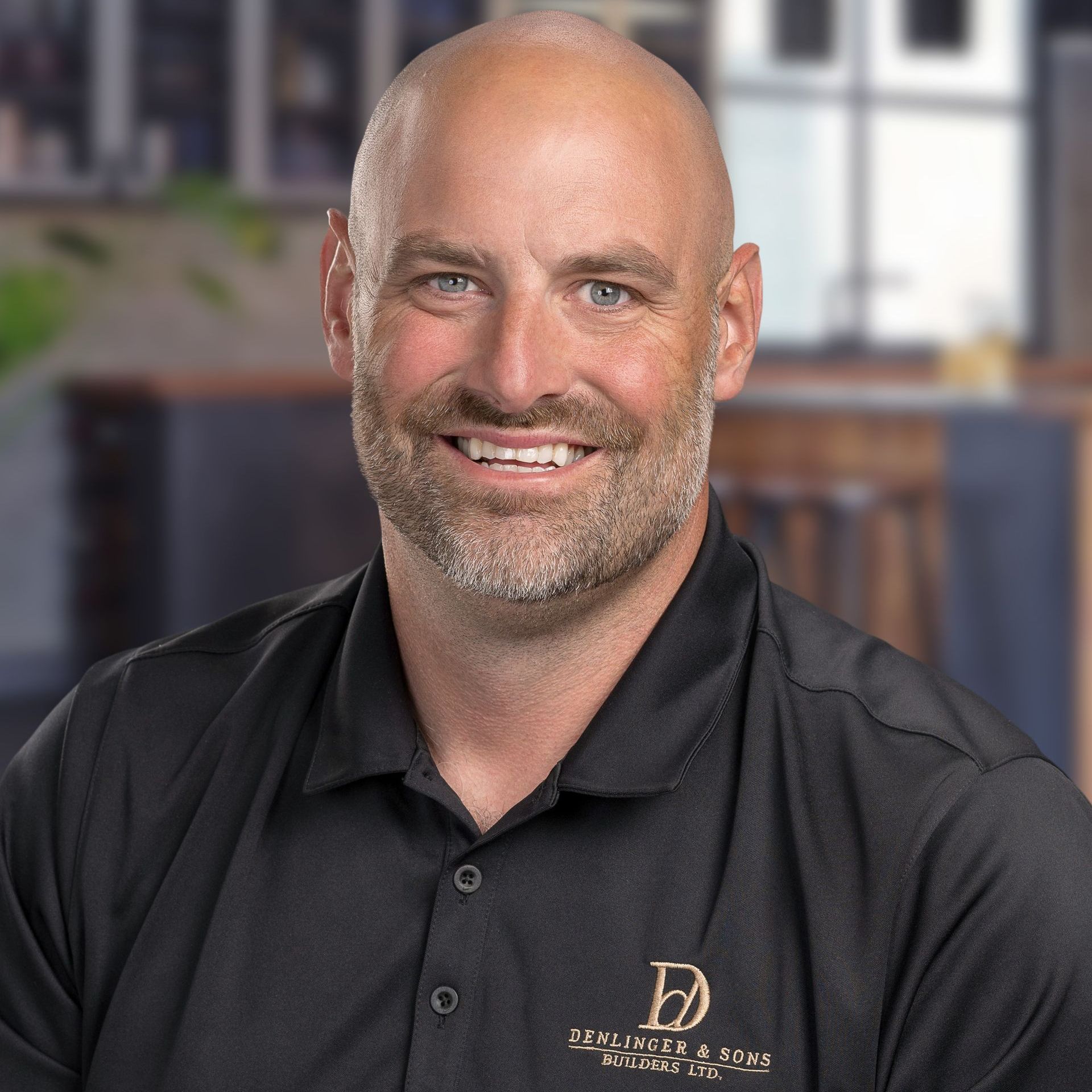 A bald man with a beard is wearing a black shirt and smiling.