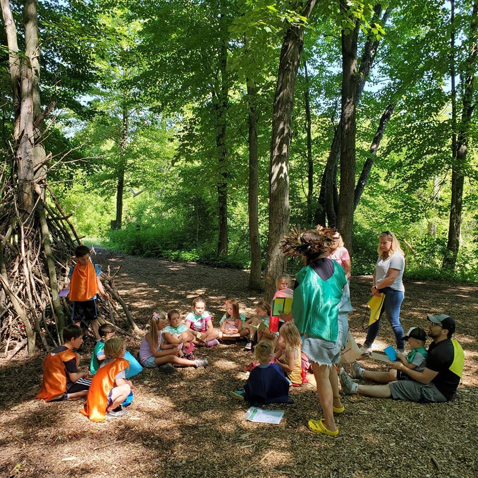A group of children are sitting on the ground in the woods.