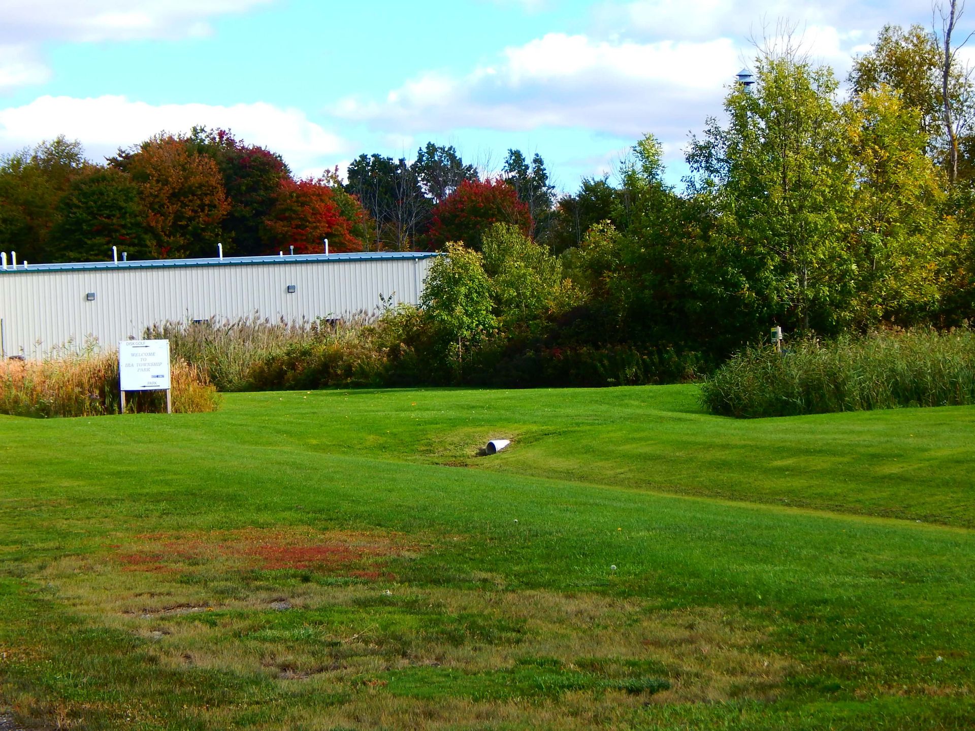 A large white building is behind a lush green field.