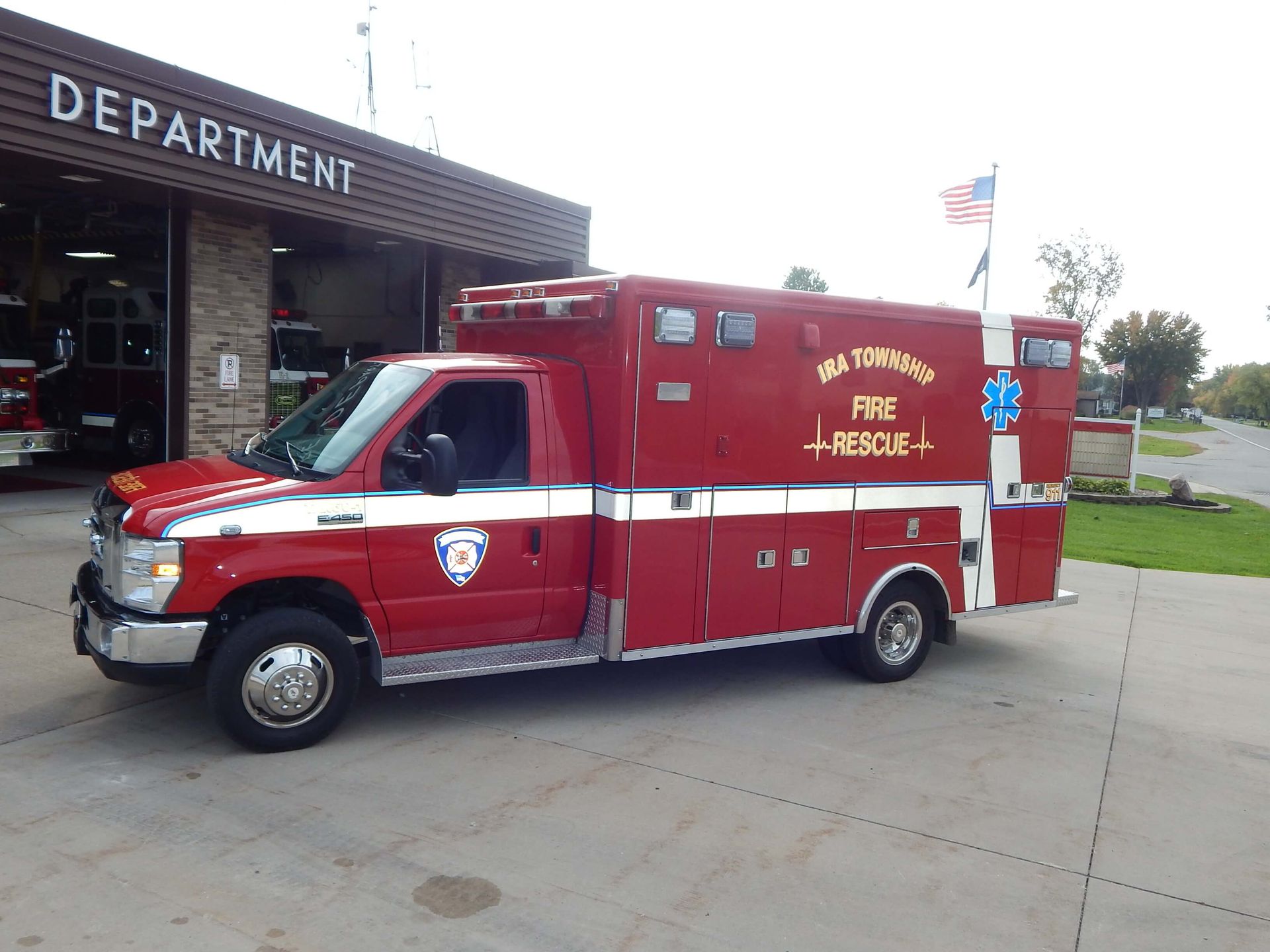 A red ambulance is parked in front of a fire department.