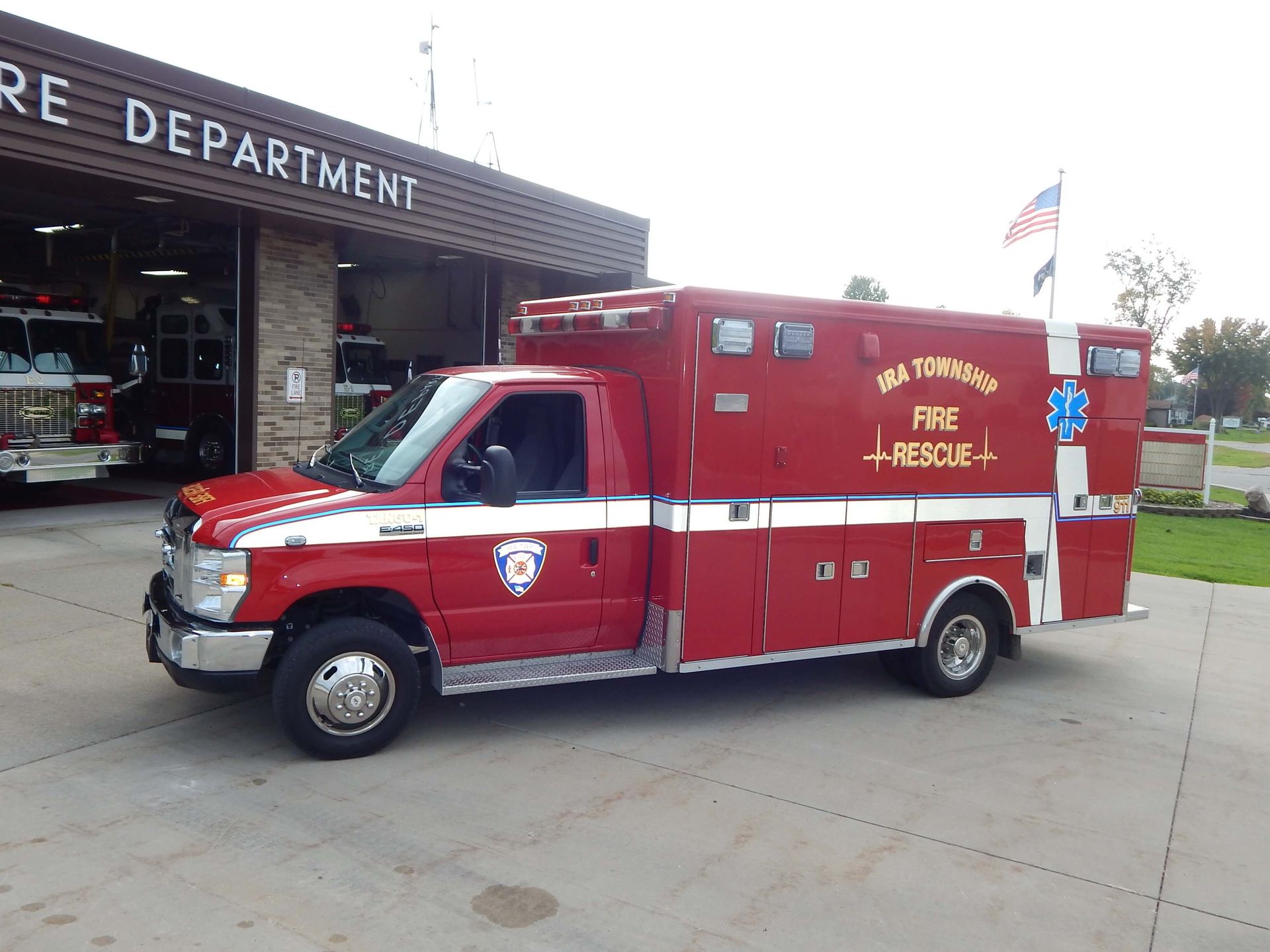 A red ambulance is parked in front of a fire department.