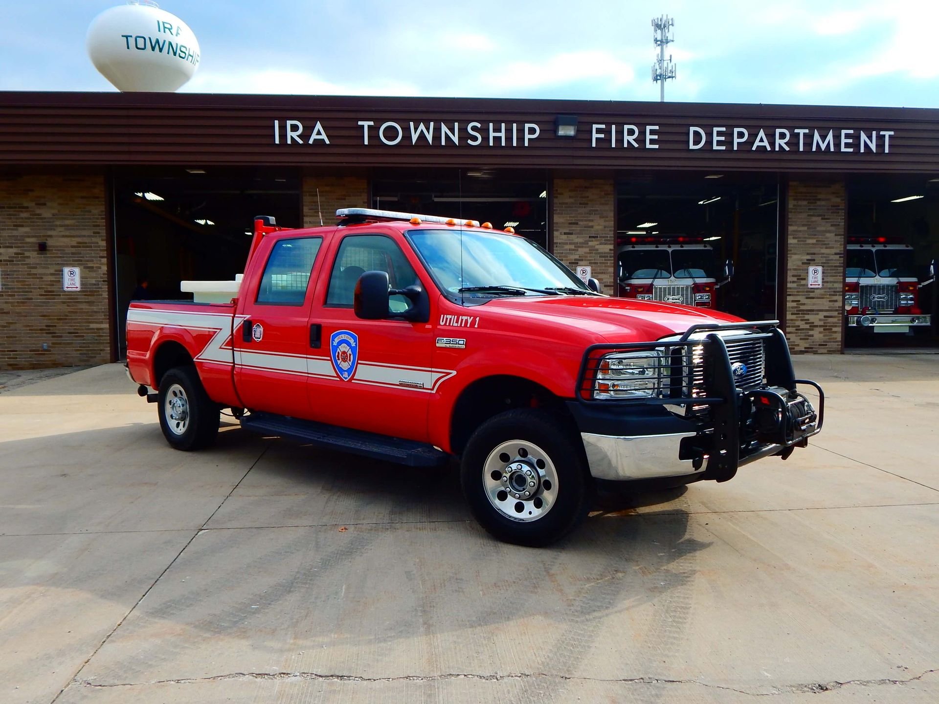 A red truck is parked in front of a building that says Ira Township Fire Department.