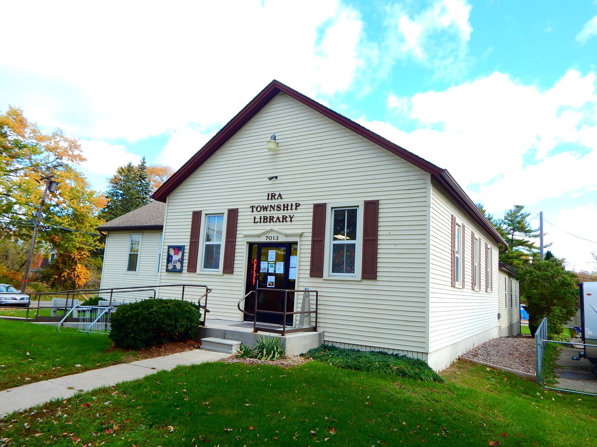 A small white building with brown shutters and a sign that says 'Ira Township Library.'