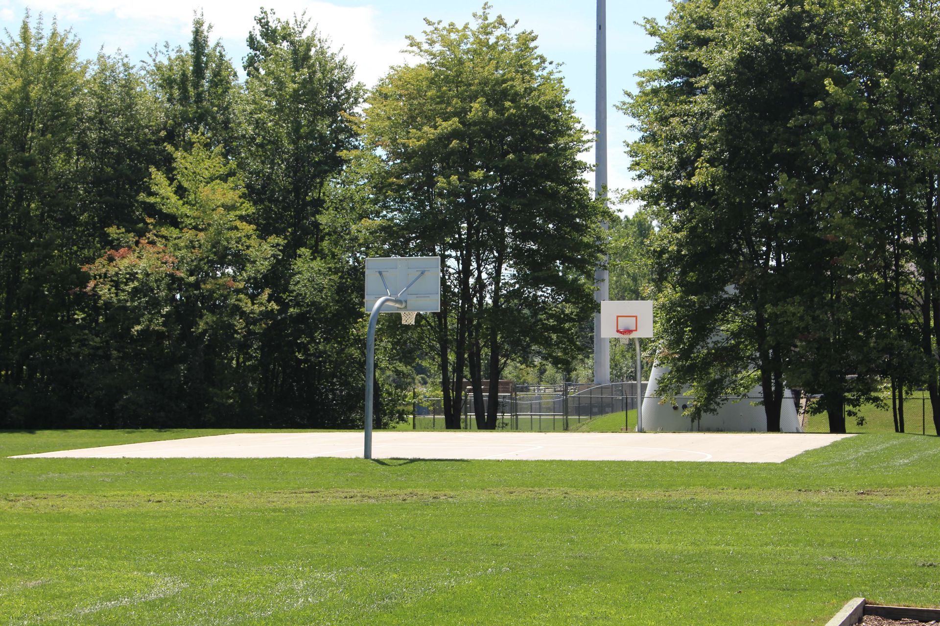 A basketball court in a park with trees in the background.