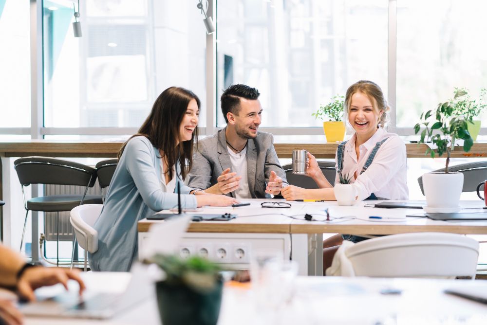 group of people are sitting at a table in an office having a conversation
