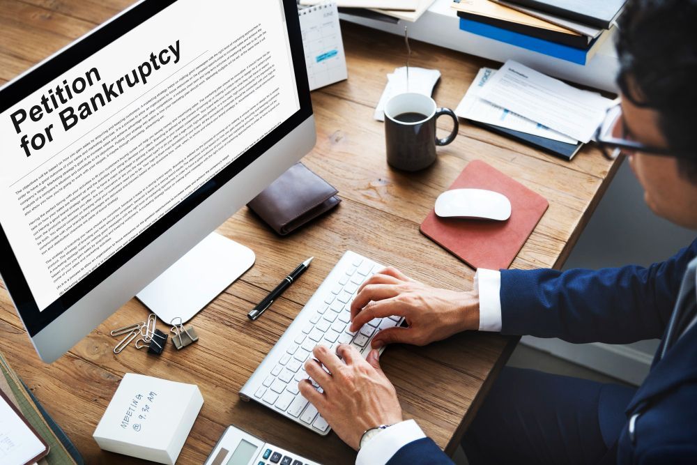 man is typing on a keyboard in front of a computer screen that says petition for bankruptcy