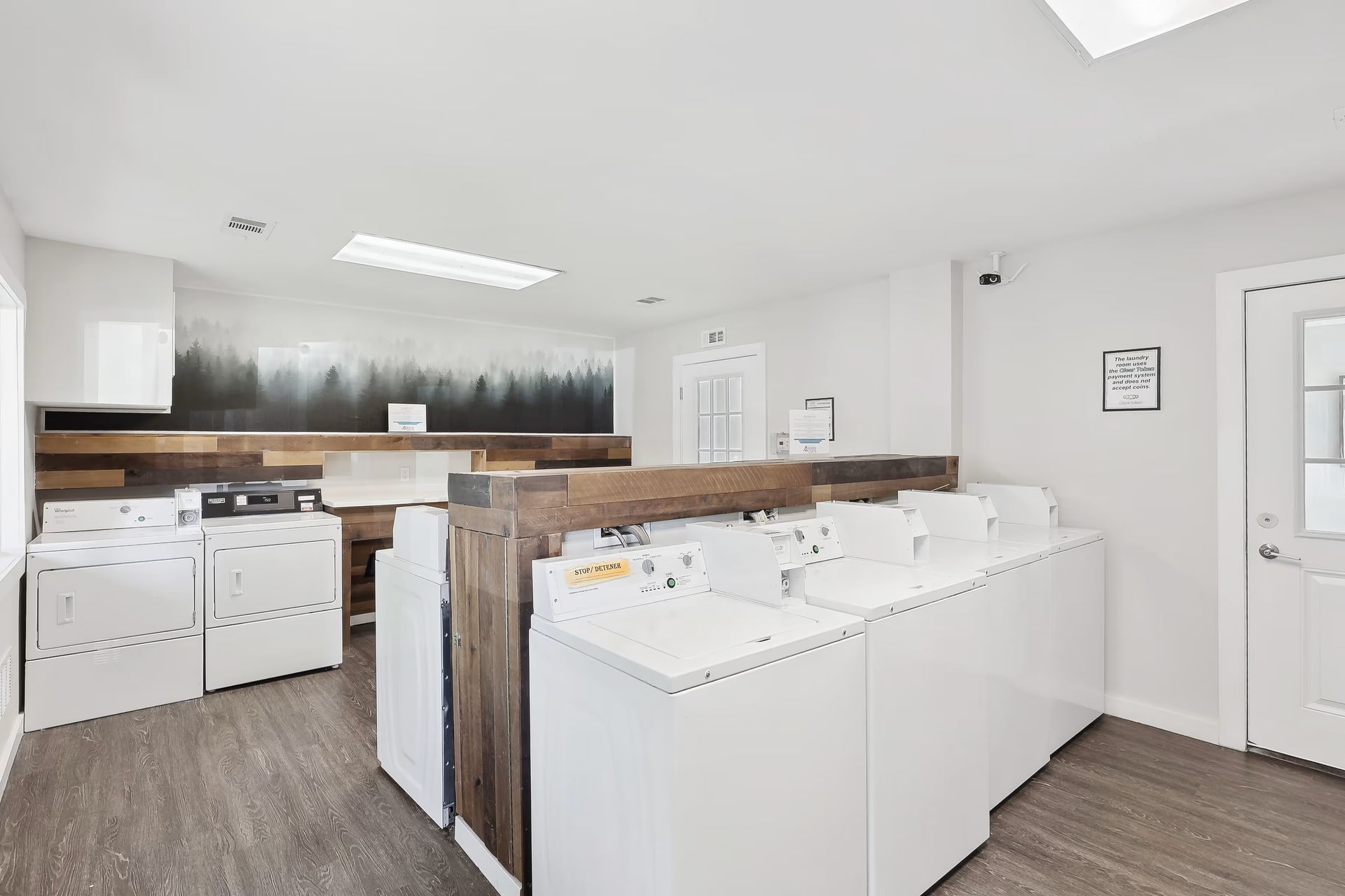 A shared laundry room featuring rows of white washing machines and dryers against a rustic wood-paneled wall at Alpine Lofts in Windsor, CO.