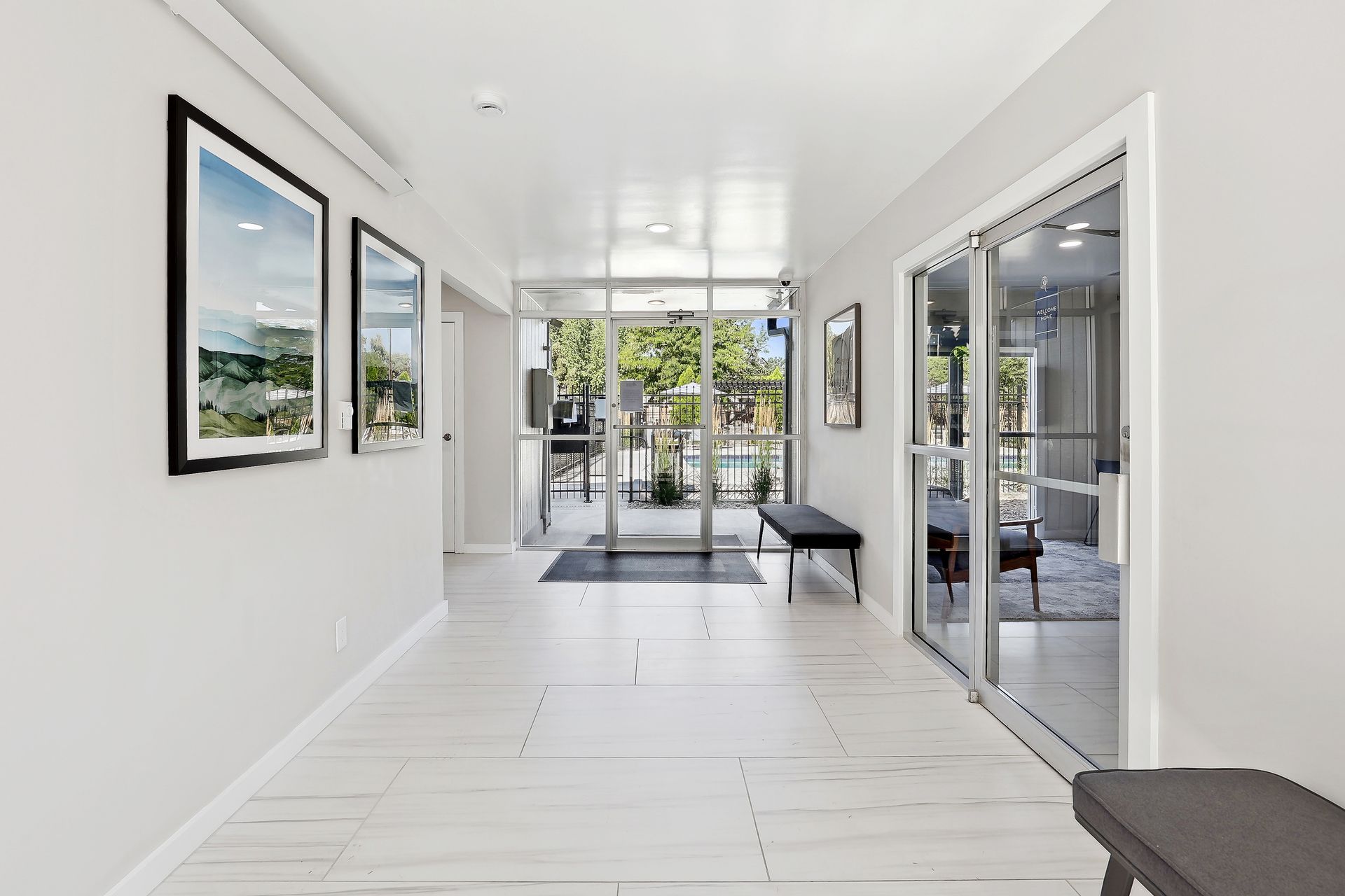 A bright, modern entryway with light flooring, two framed prints on the left wall, and glass double doors to the right at Alpine Lofts in Windsor, CO.