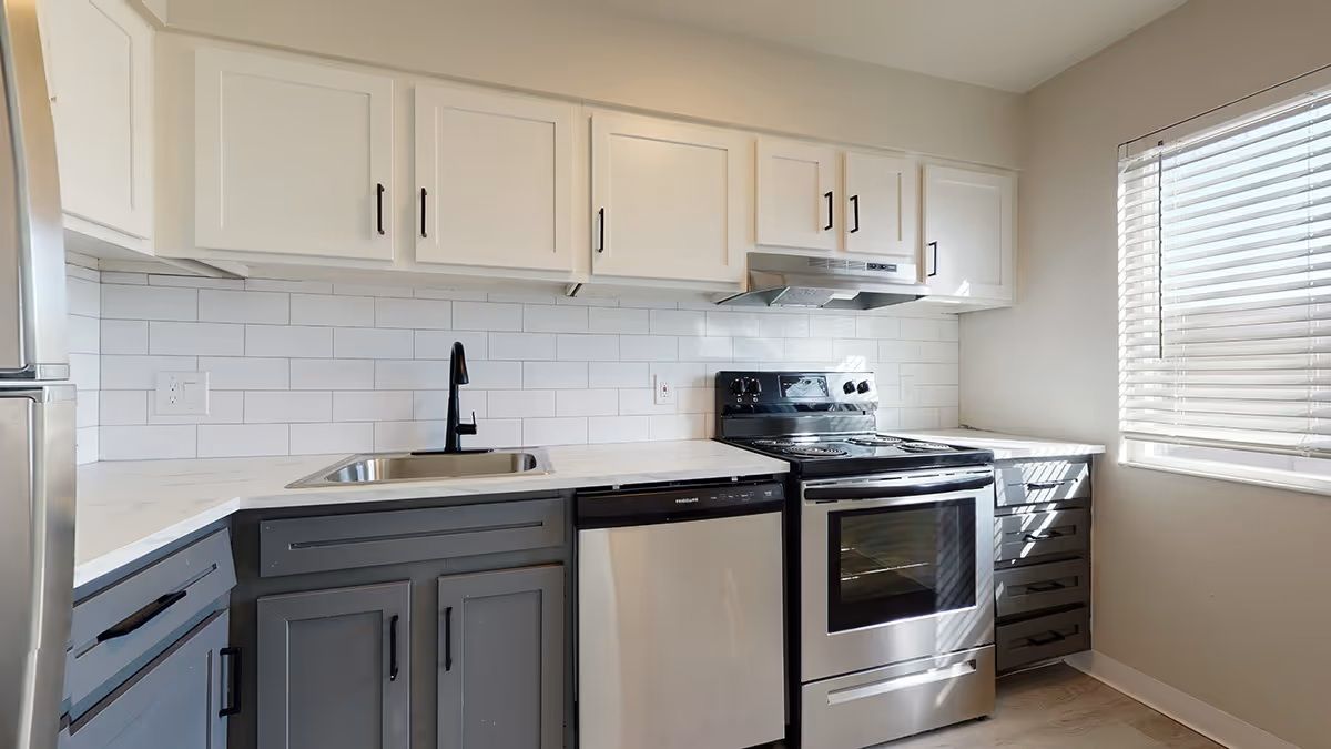 Modern kitchen with white upper cabinets, grey lower cabinets, subway tile backsplash, and stainless steel appliances at Alpine Lofts in Windsor, CO.
