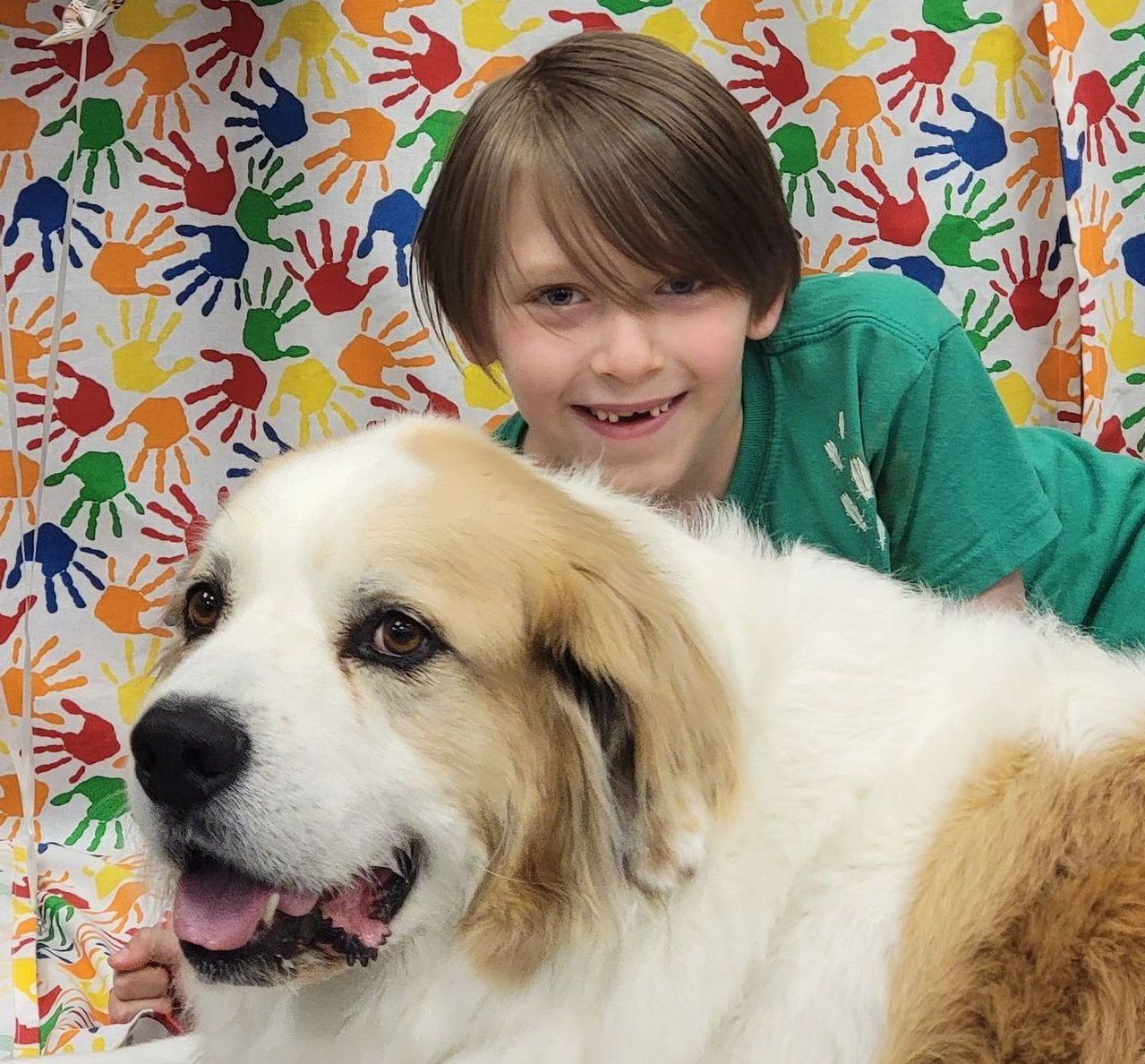 A boy in a green shirt is laying next to a brown and white dog