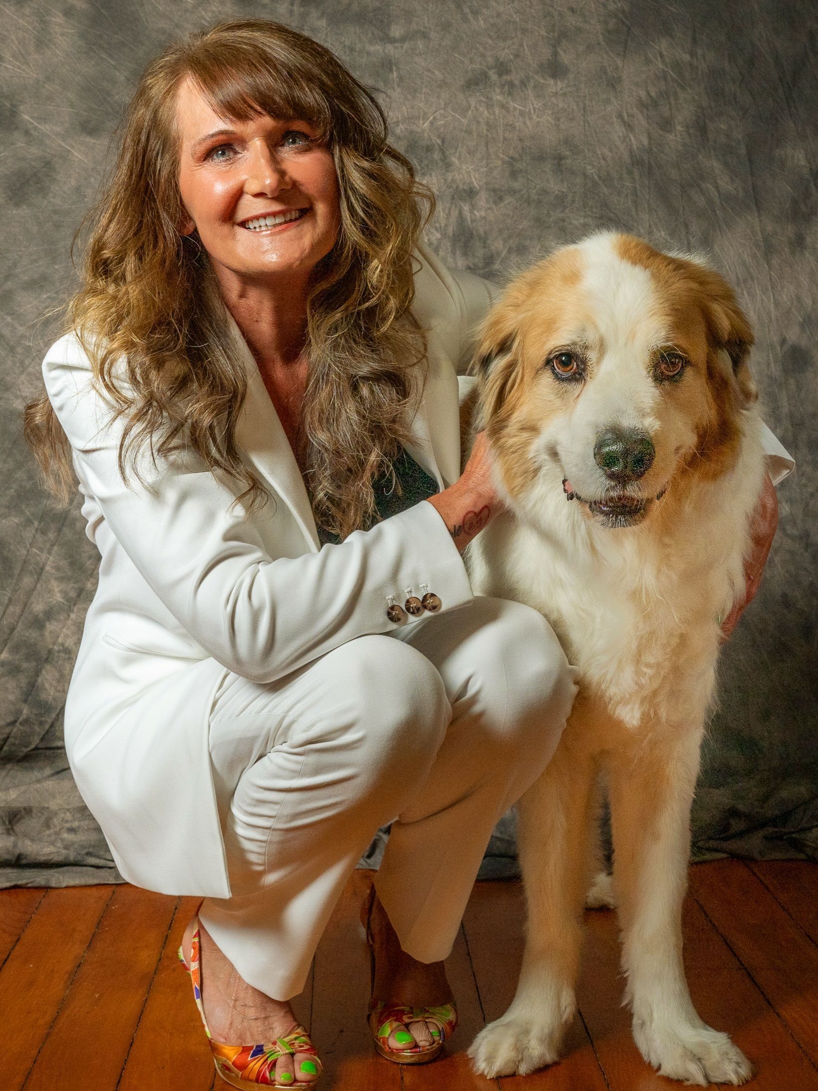 A woman in a white suit is kneeling down next to a brown and white dog.