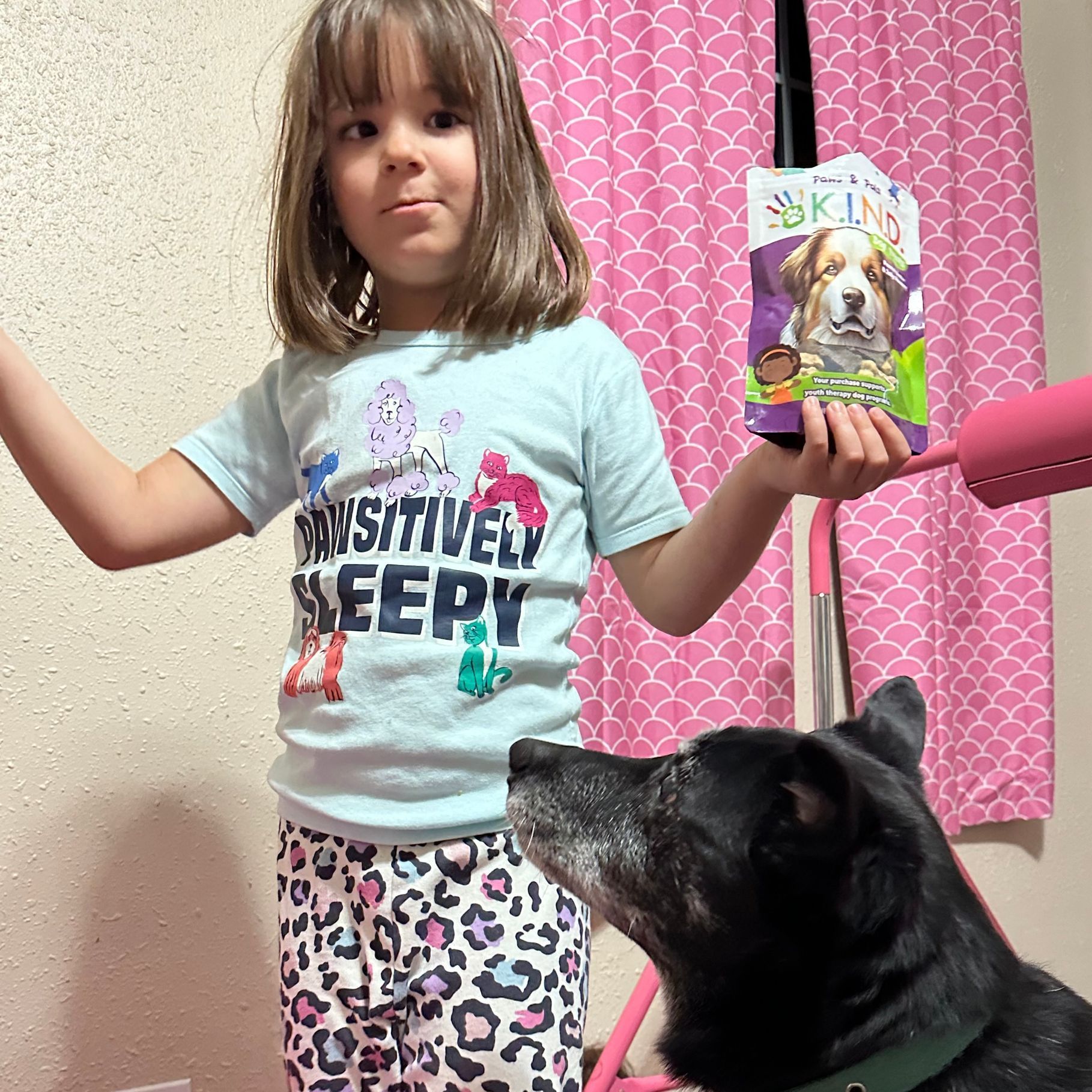 A little girl is standing next to a dog holding a bag of dog food.