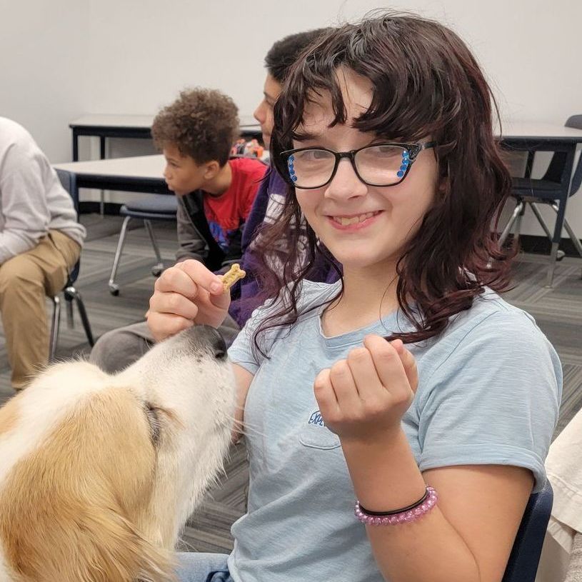 A girl with glasses is feeding a dog a treat.