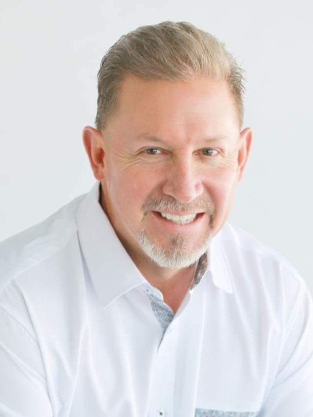 A man with a beard is wearing a white shirt and smiling.