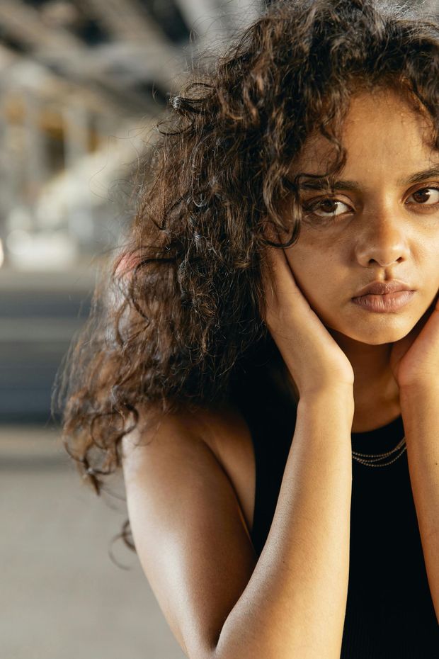 A young woman with curly hair is sitting down with her hands on her face.