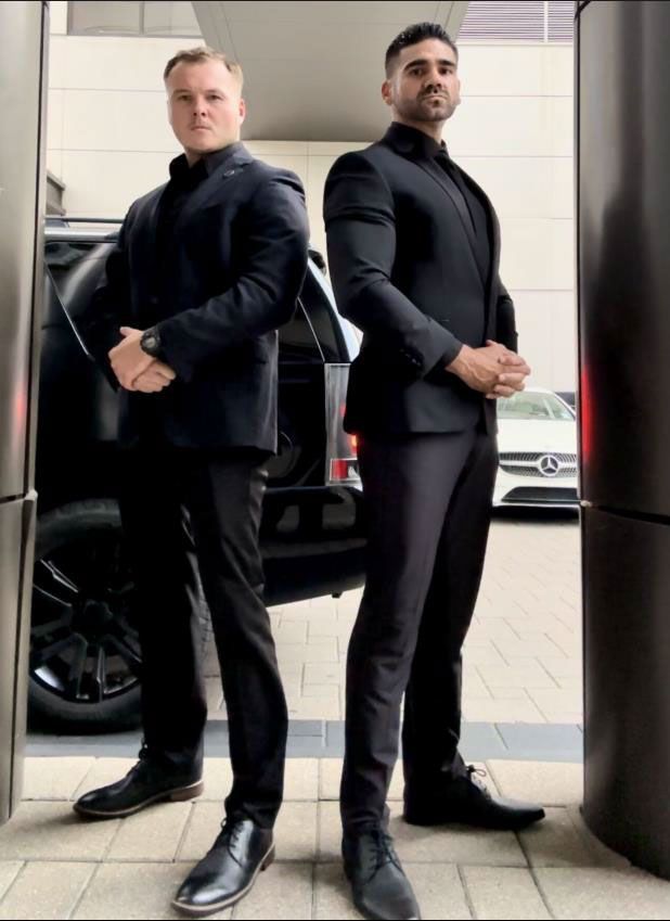 Man in black suit stands by a black car with a yellow energy arc in Monaco.