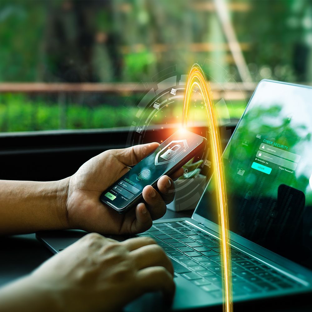 Person using laptop and smartphone with a glowing data transfer visualization.