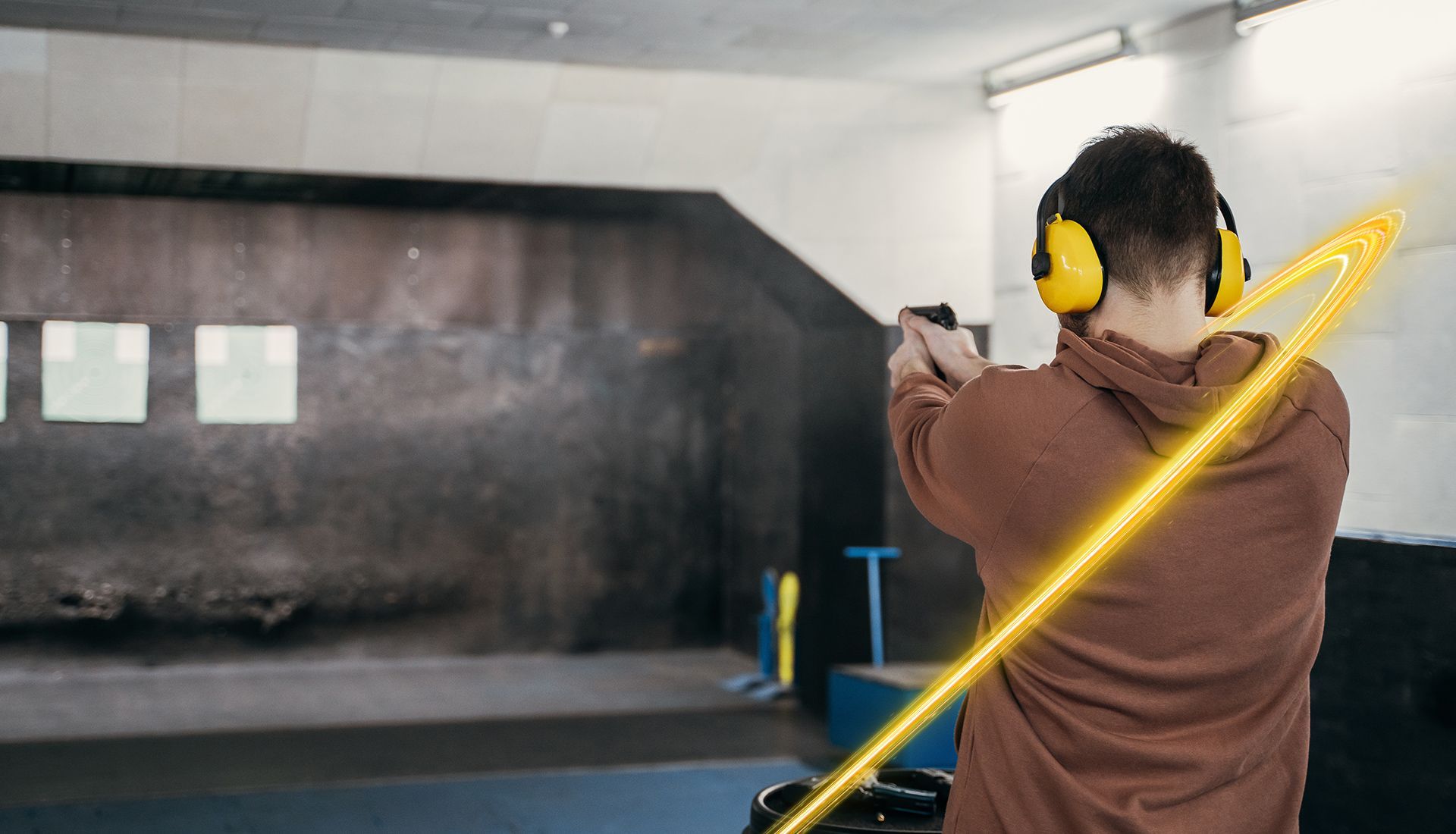 Man in ear protection aiming a handgun at a shooting range target.