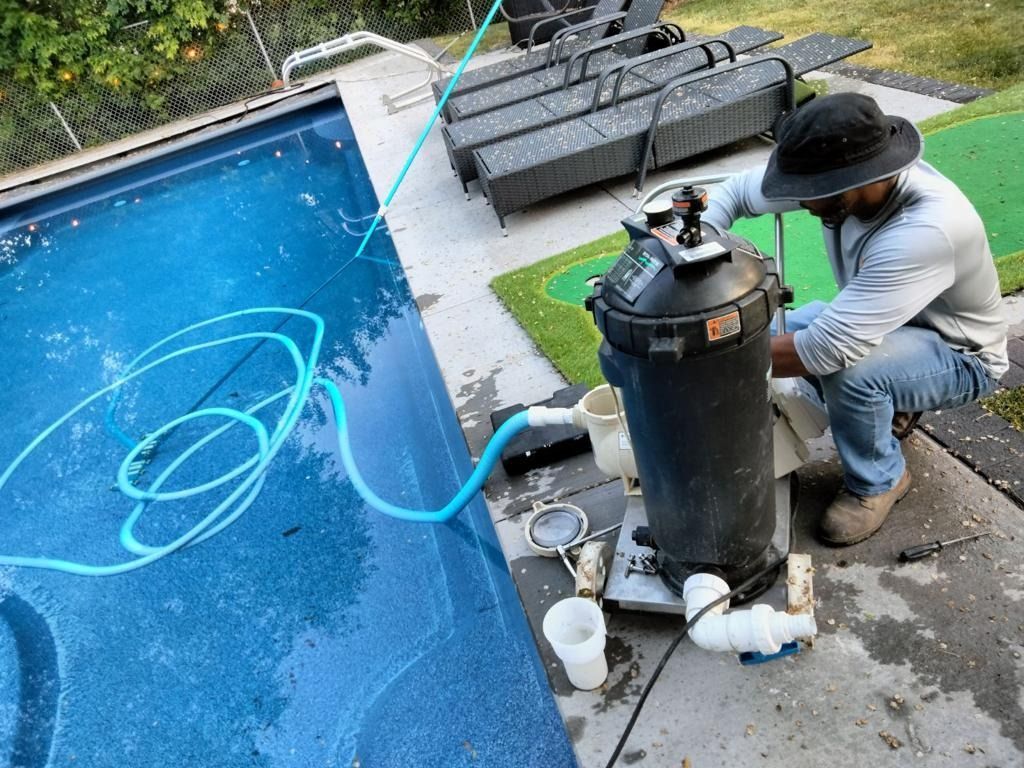 Man servicing pool filter near a pool, using blue hose and tools.