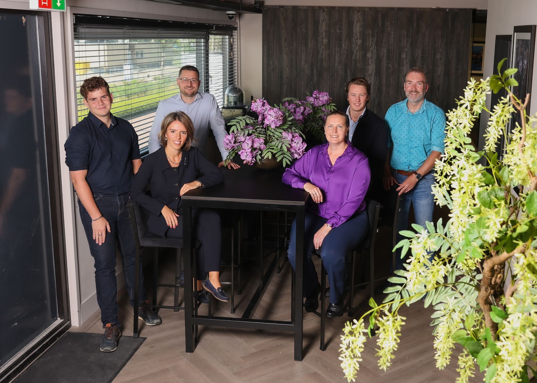 Een groep mensen die rond een tafel zitten met bloemen erop