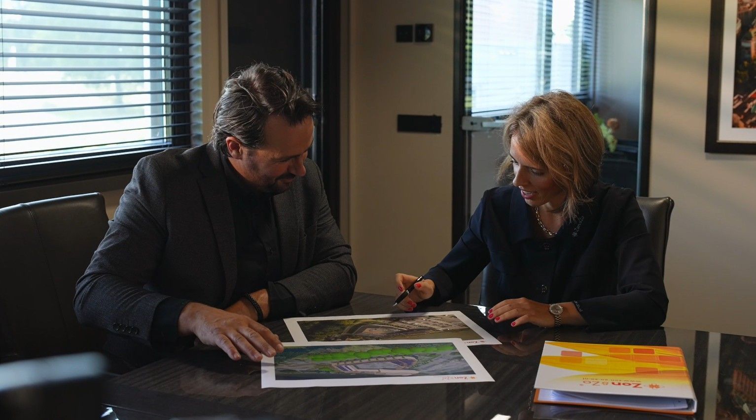 Een man en een vrouw zitten aan een tafel en kijken naar een laptop.