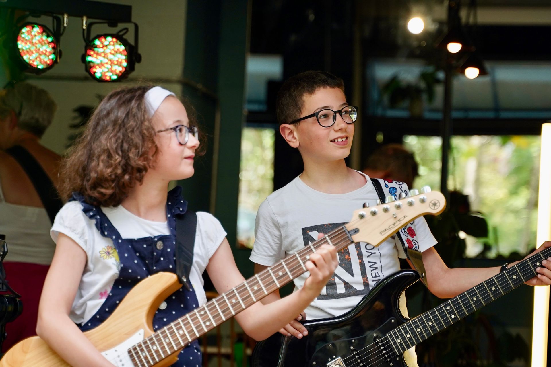 A boy and a girl are playing guitars on a stage.