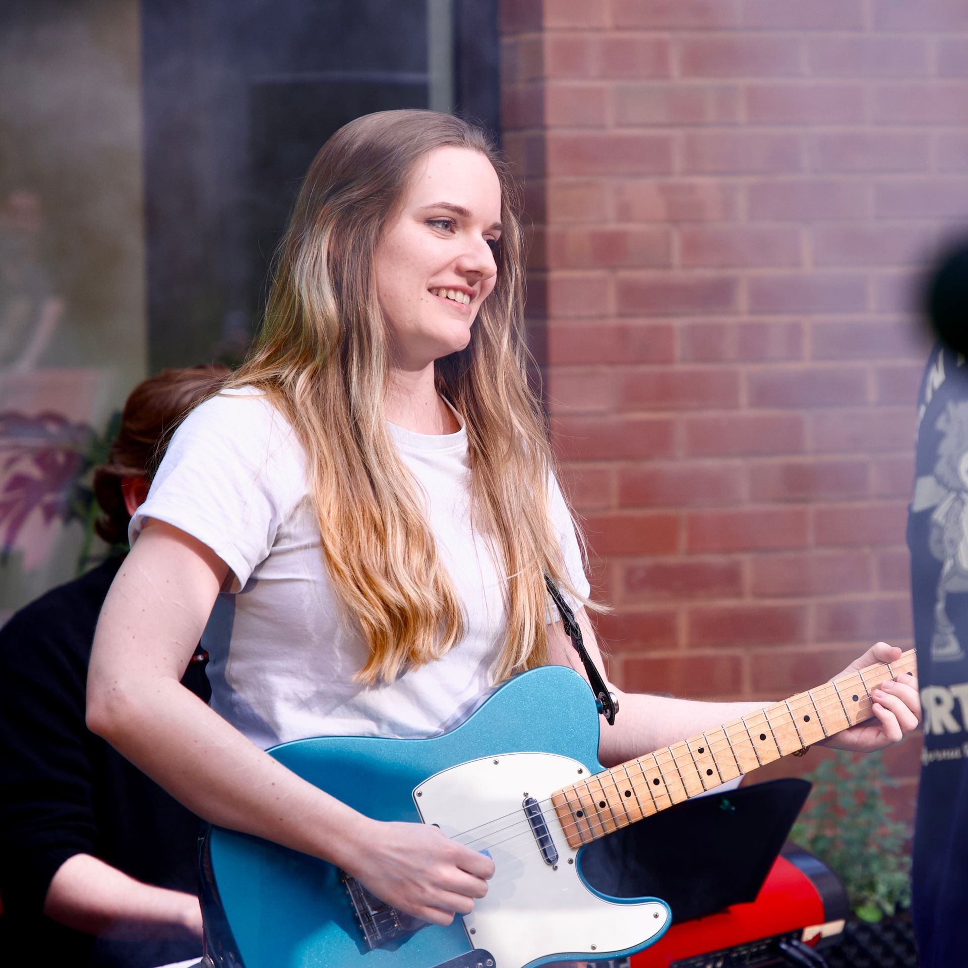 A woman is playing a blue electric guitar in front of a brick wall