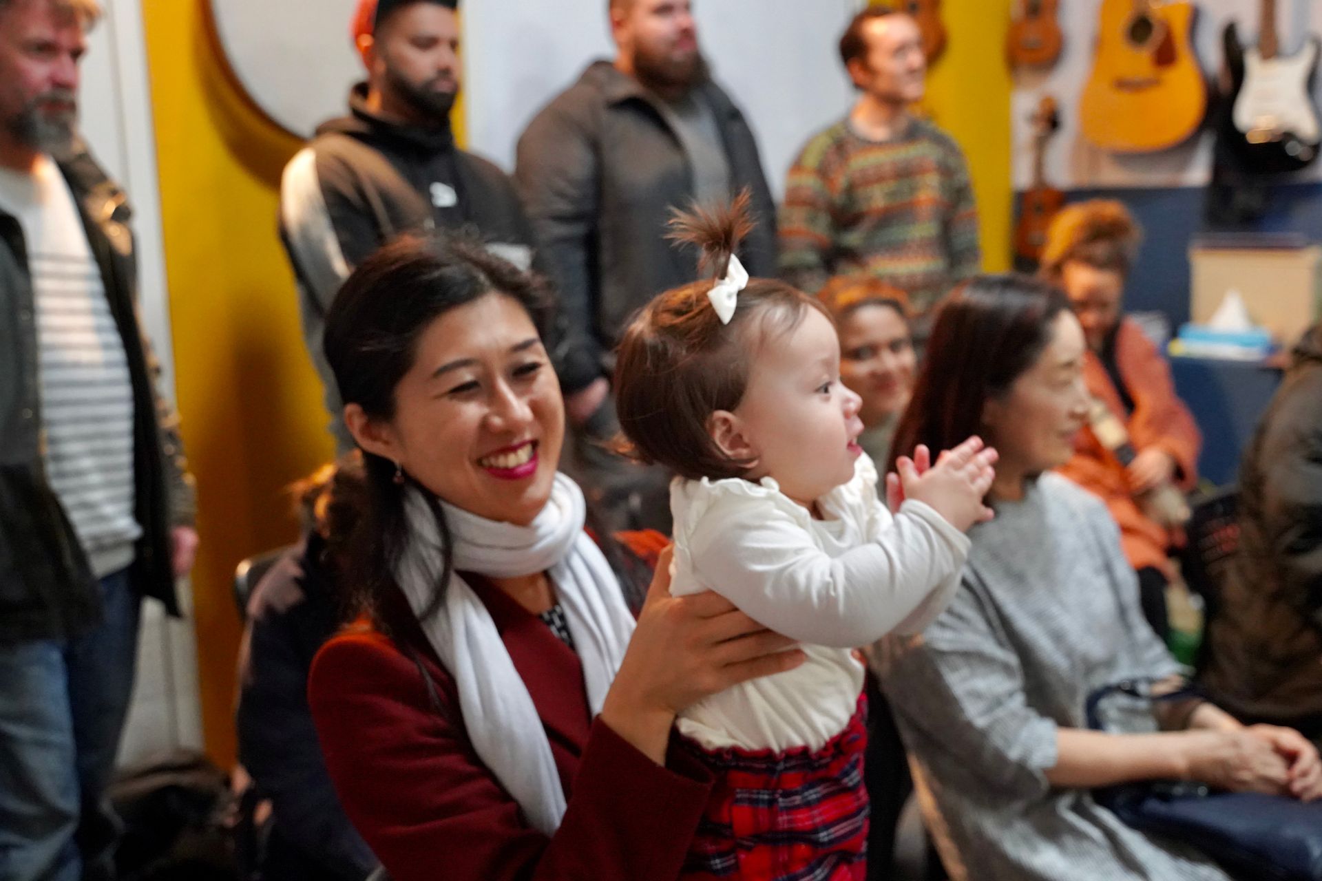 A woman is holding a baby in her arms in front of a group of people.