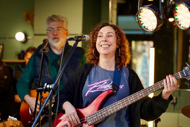 A woman is playing a bass guitar and singing into a microphone.