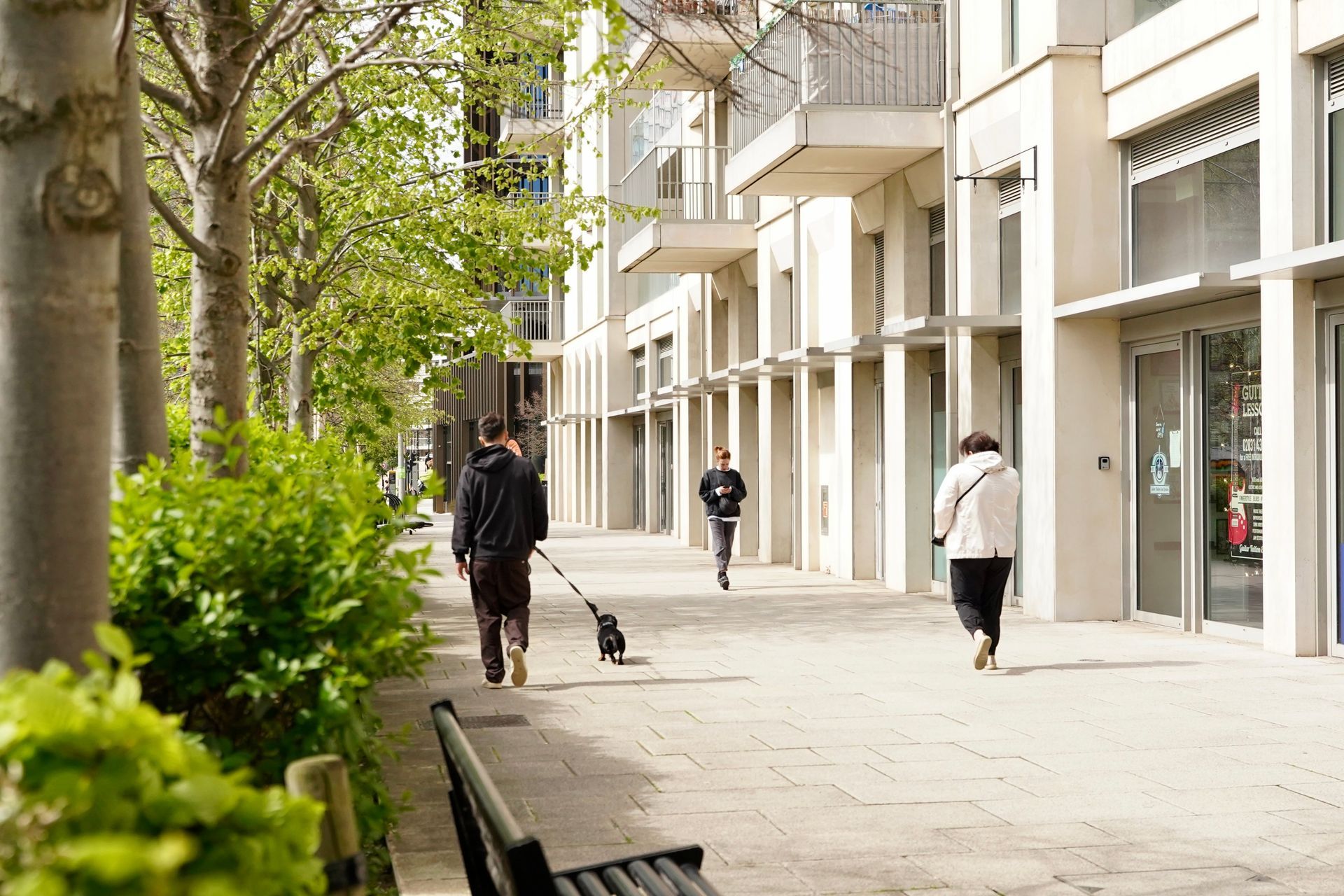 A man is walking a dog on a leash down a sidewalk in front of a building.
