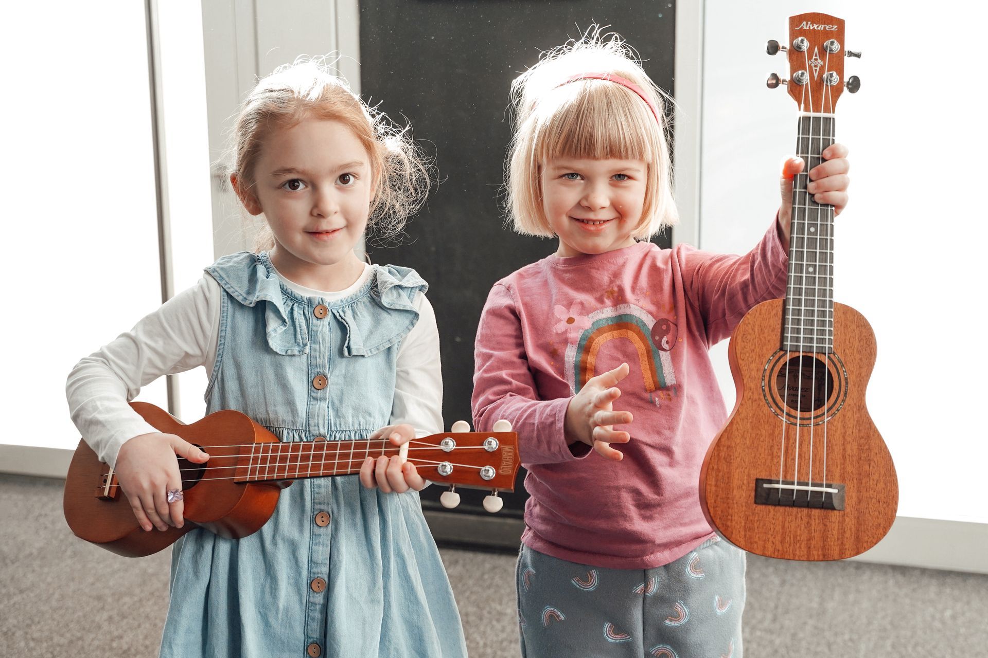 Two little girls are holding ukuleles in their hands.