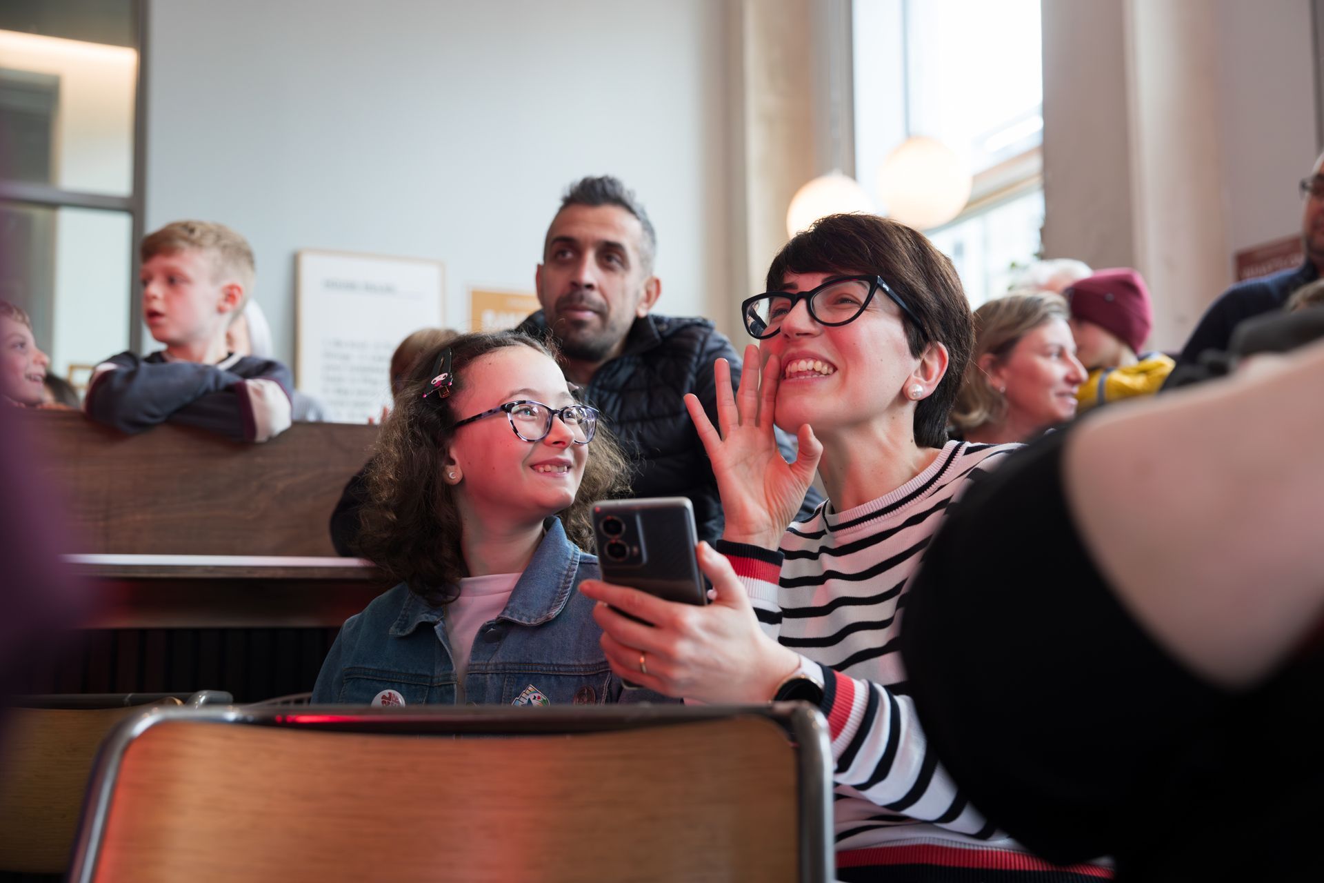 A woman is holding a cell phone in her hand while sitting in a classroom.