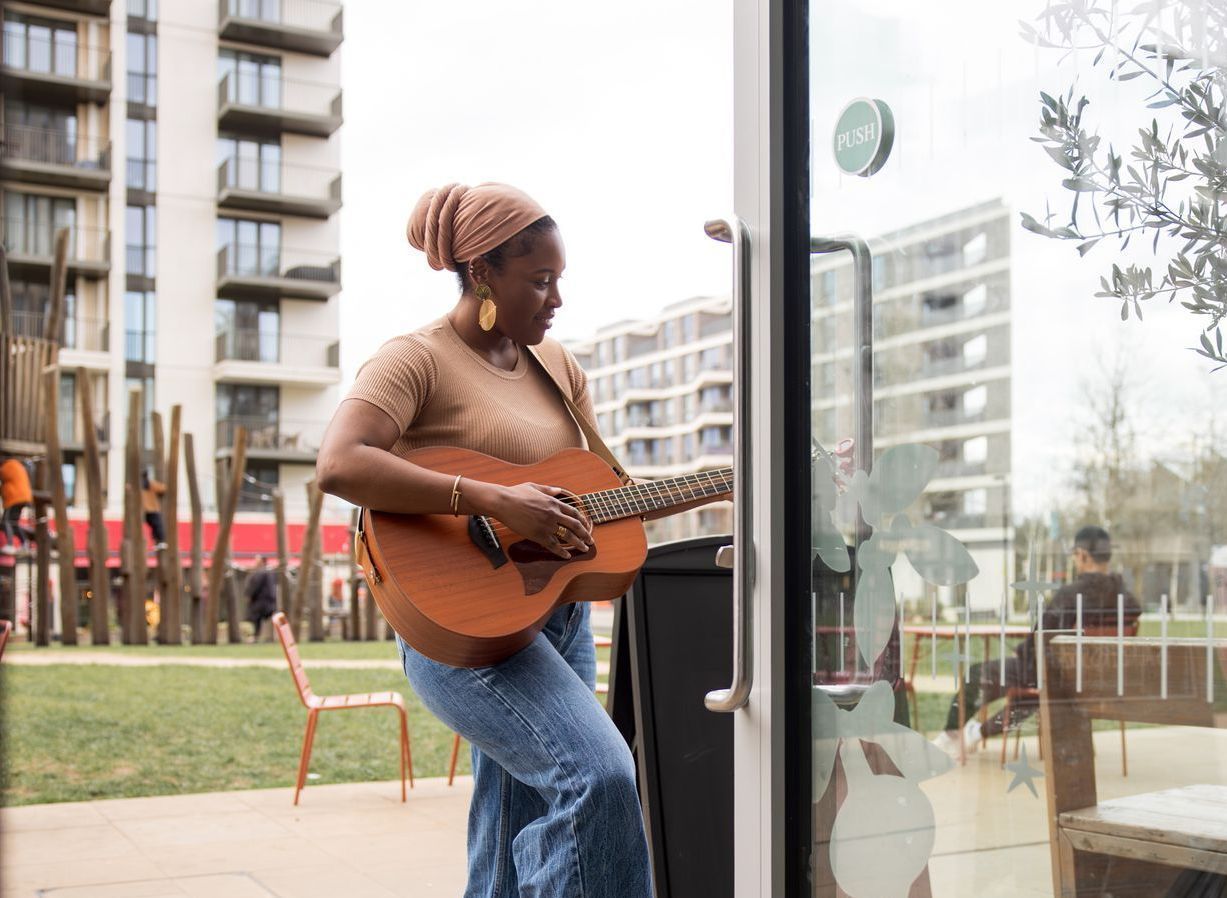 A woman is tuning her guitar outside a cafe before her performance.