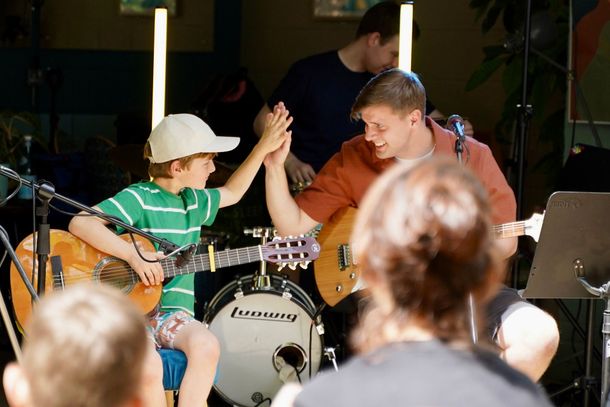 A man and a boy are giving each other a high five while playing guitars.
