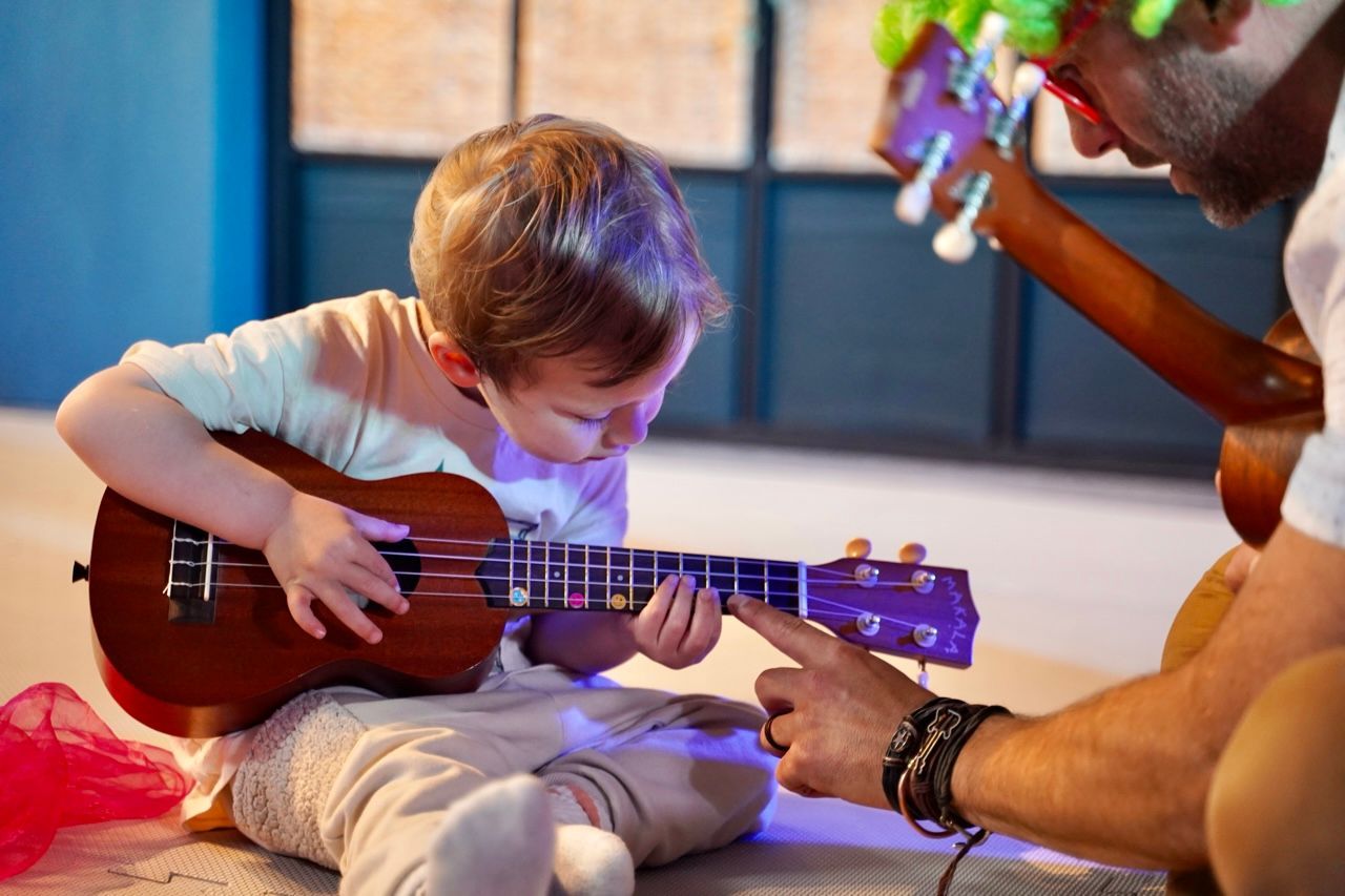 A man is teaching a young boy how to play a ukulele.