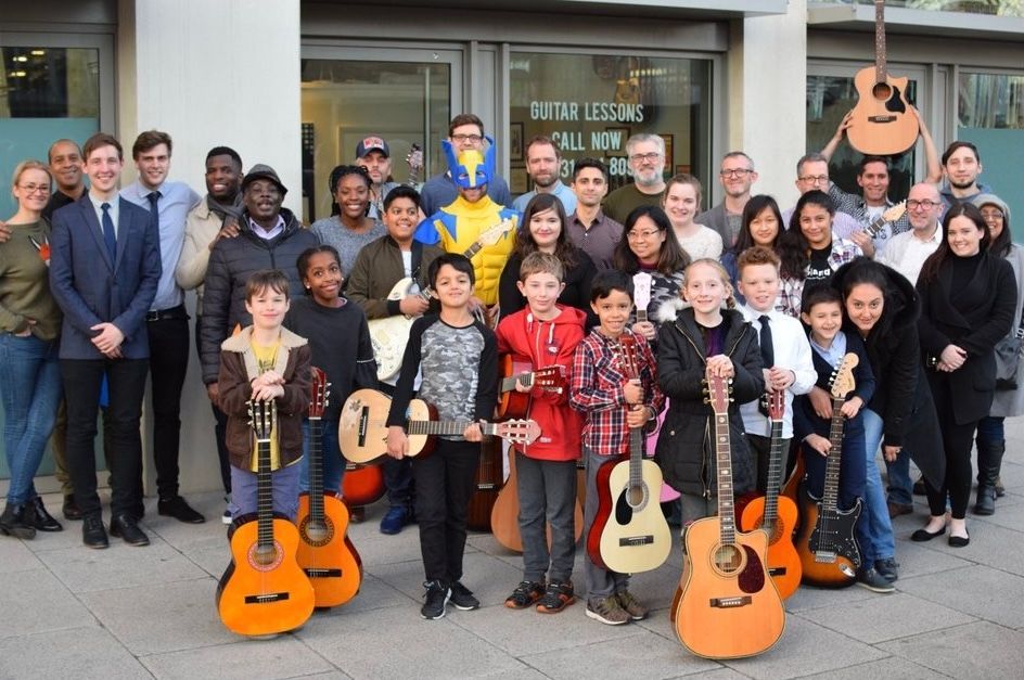 A group of people standing in front of a building holding guitars.