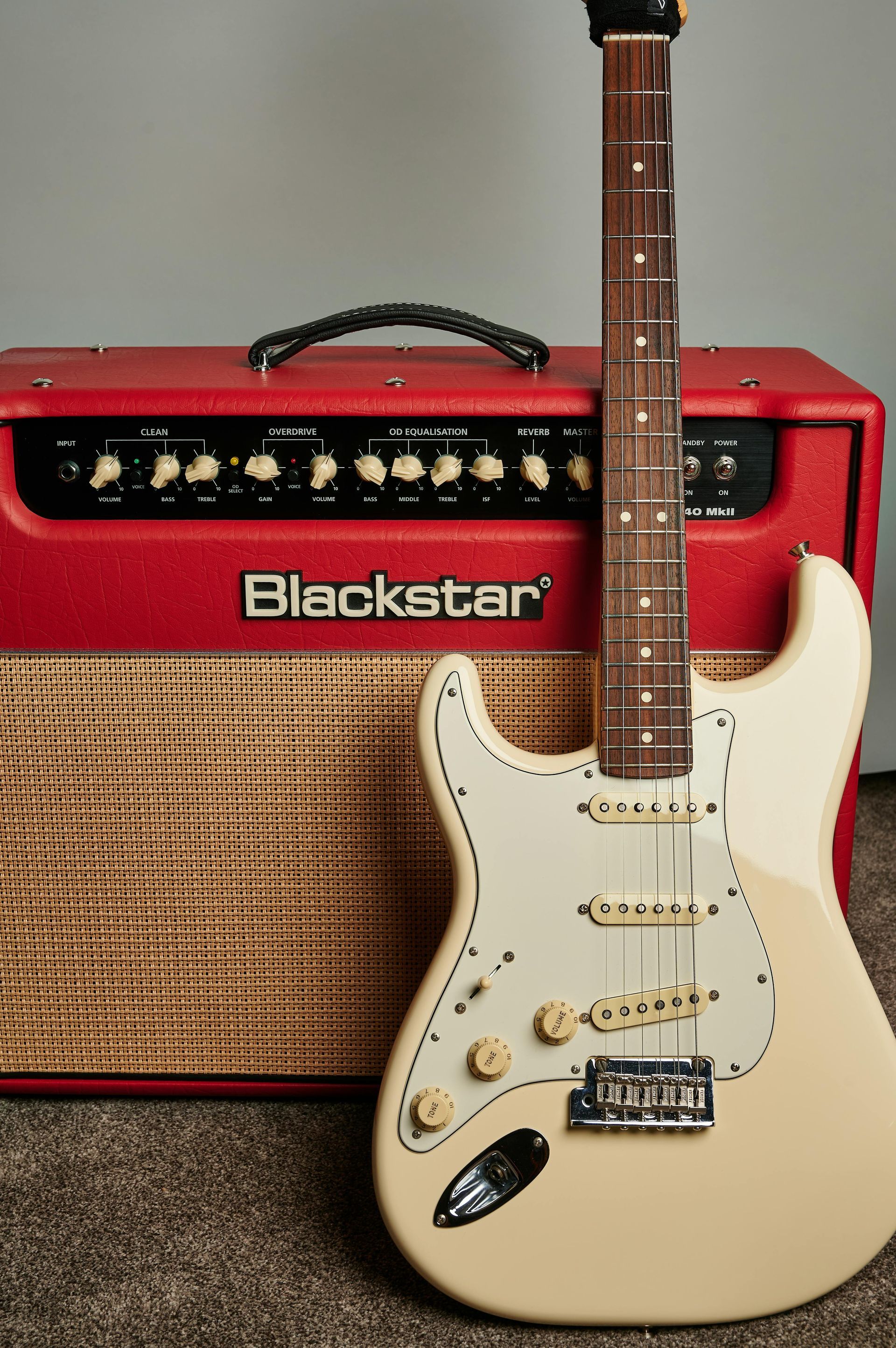 A white electric guitar is sitting next to a red blackstar amplifier
