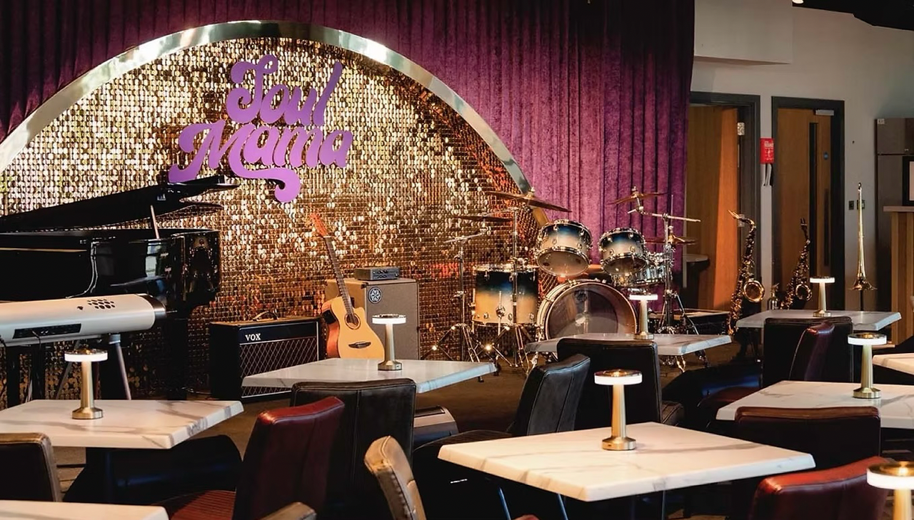 A restaurant with tables and chairs in front of a stage with a piano and drums.