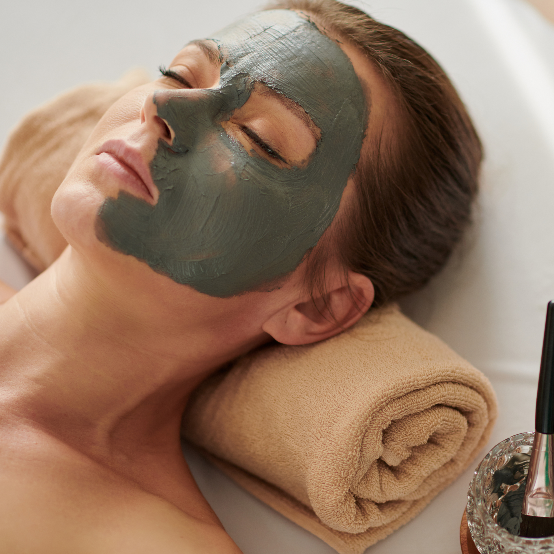 A woman with a green mask on her face is laying on a towel