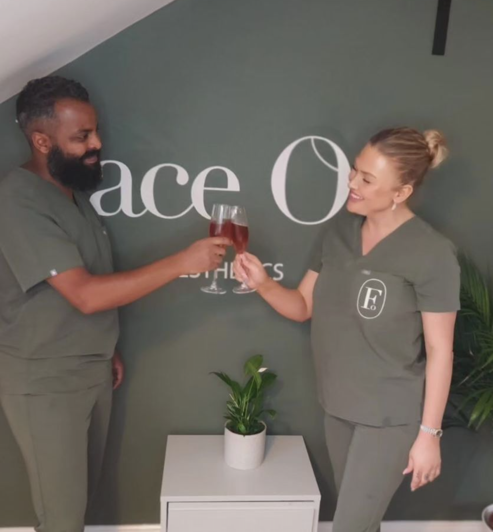 A man and a woman toasting in front of a wall that says ace